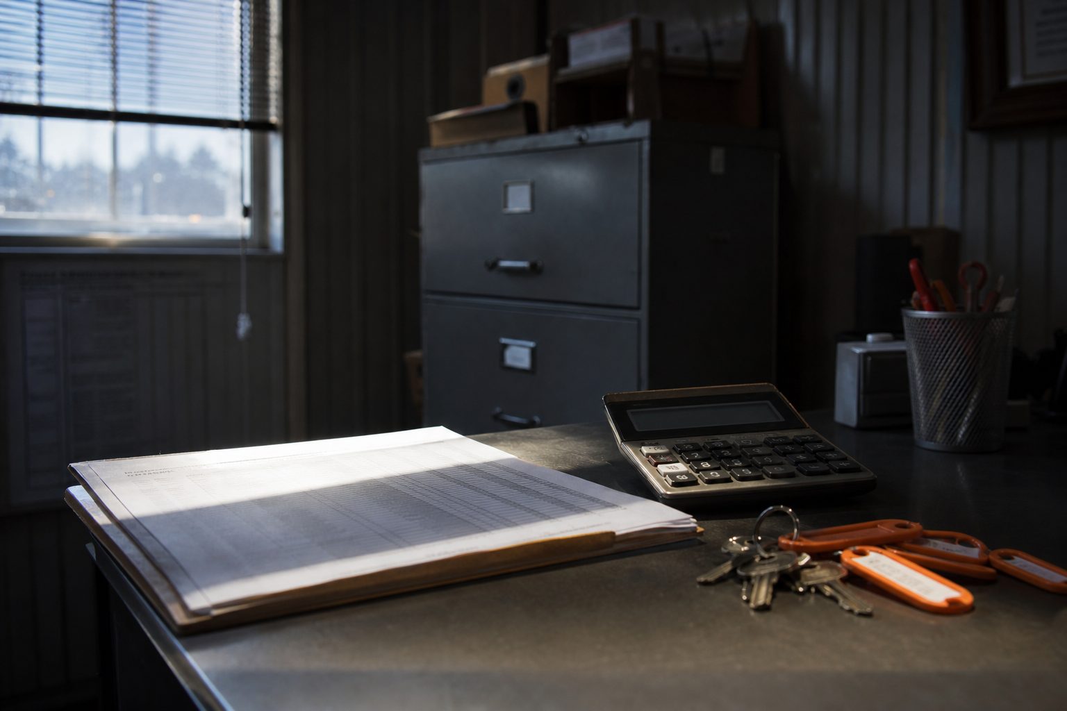 Storage office desk with a printed tenant list, a calculator and a ring of orange tagged unit keys
