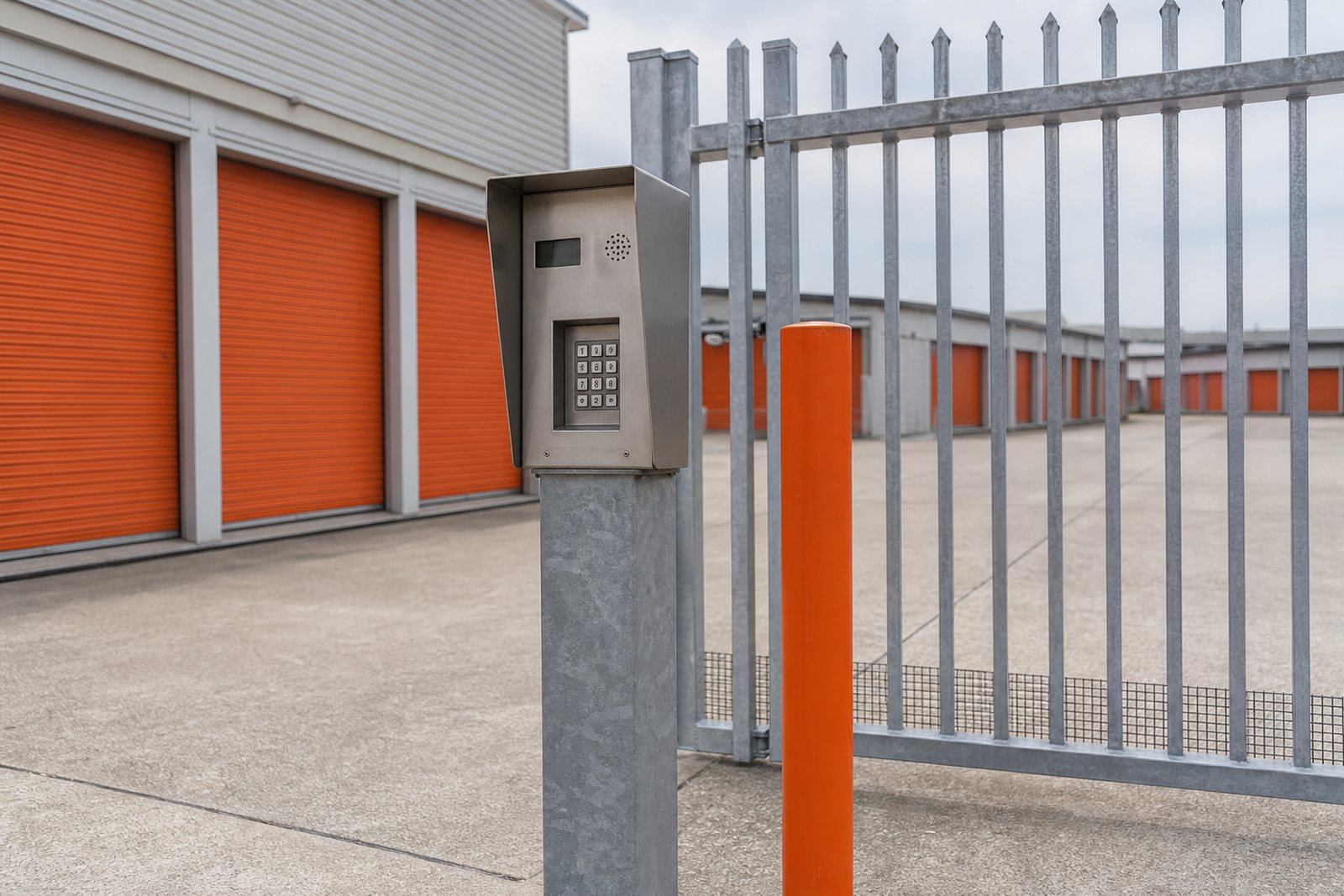 Keypad entry post and security gate at the driveway of a self storage property under overcast light